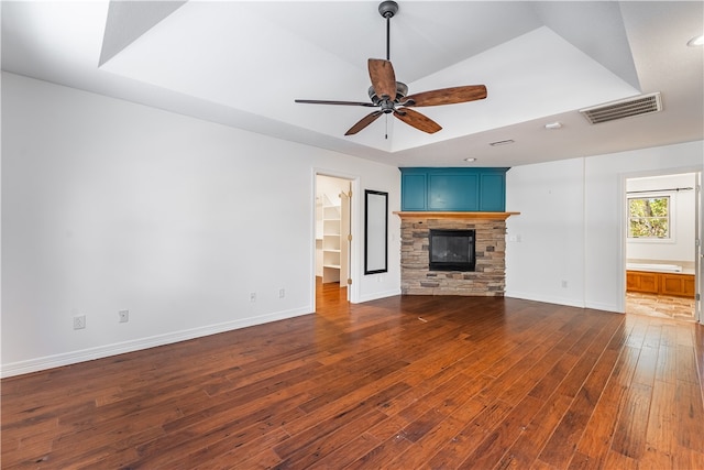 unfurnished living room with a stone fireplace, ceiling fan, a raised ceiling, and dark hardwood / wood-style flooring