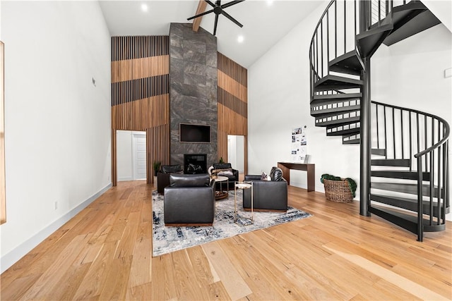 living room with hardwood / wood-style flooring, high vaulted ceiling, a tile fireplace, baseboards, and stairs