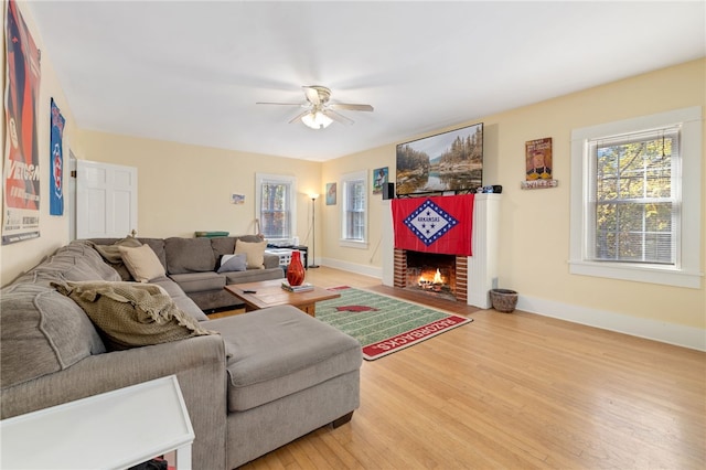 living area featuring a fireplace, light wood-style flooring, a ceiling fan, and baseboards