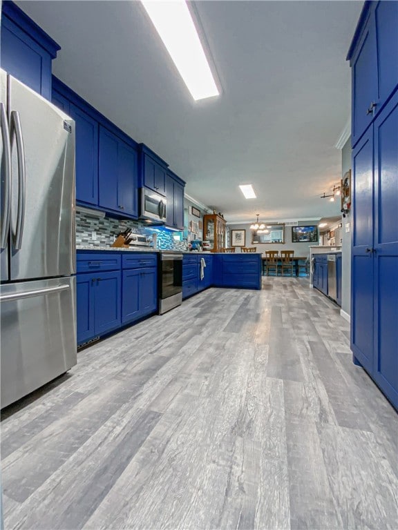 kitchen with appliances with stainless steel finishes, kitchen peninsula, blue cabinetry, a notable chandelier, and decorative backsplash