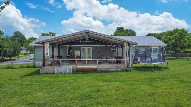 back of property with french doors, a deck, a yard, and a trampoline