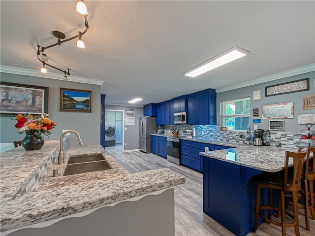 kitchen with kitchen peninsula, ornamental molding, stainless steel appliances, sink, and blue cabinets