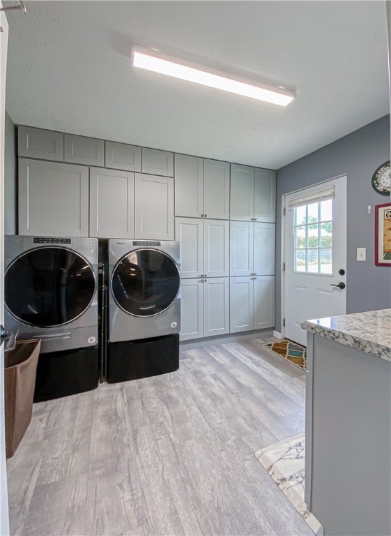 laundry room with washing machine and clothes dryer, light hardwood / wood-style floors, and cabinets