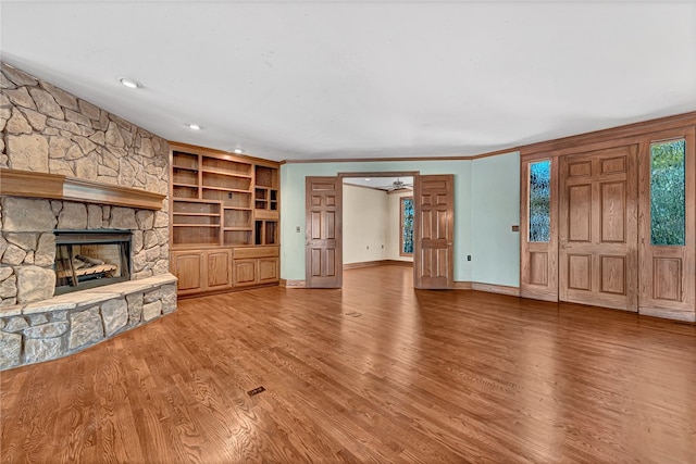 unfurnished living room featuring a stone fireplace, ornamental molding, and wood-type flooring