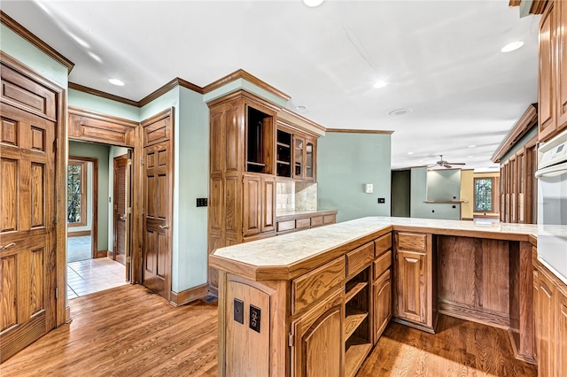 kitchen with white oven, ceiling fan, light wood-type flooring, ornamental molding, and a center island