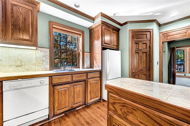 kitchen with tile counters, white appliances, ornamental molding, sink, and light hardwood / wood-style floors