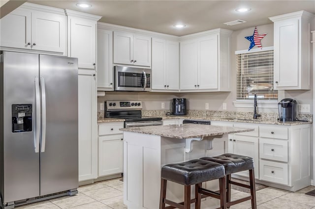 kitchen featuring light tile patterned floors, a kitchen island, a kitchen bar, stainless steel appliances, and light stone counters