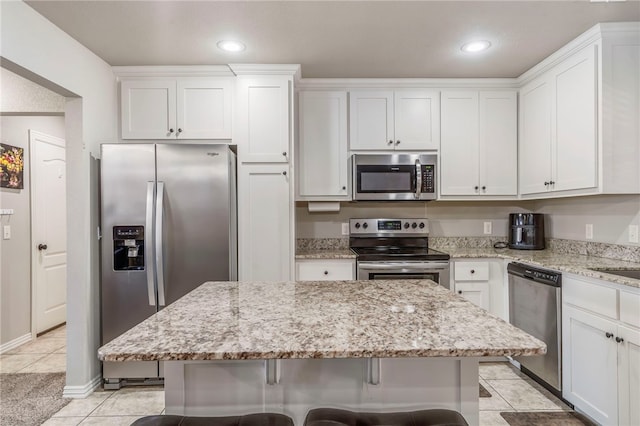 kitchen featuring stainless steel appliances, a center island, light tile patterned floors, white cabinets, and light stone counters