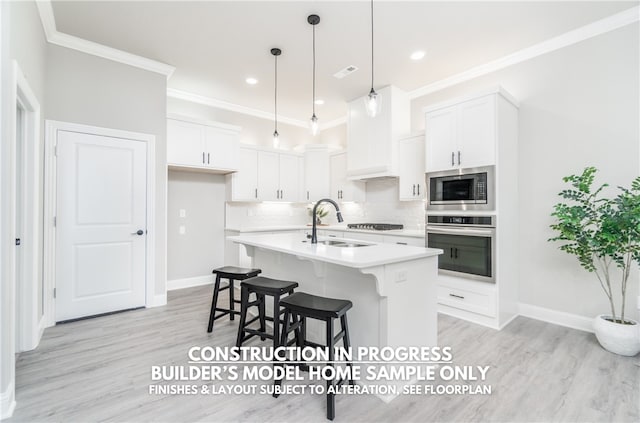 kitchen with appliances with stainless steel finishes, pendant lighting, an island with sink, and white cabinets