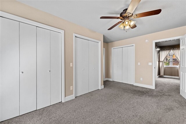 unfurnished bedroom featuring two closets, ceiling fan, and carpet flooring