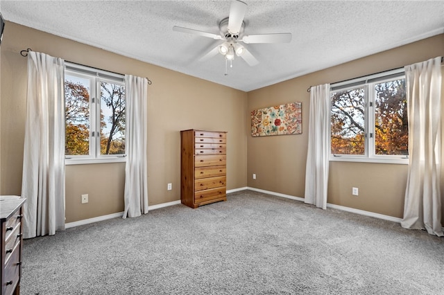 unfurnished bedroom with multiple windows, ceiling fan, light carpet, and a textured ceiling