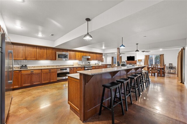 kitchen with pendant lighting, a breakfast bar area, appliances with stainless steel finishes, a center island, and light stone counters