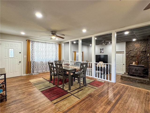 dining room featuring wood-type flooring, a wood stove, and ceiling fan