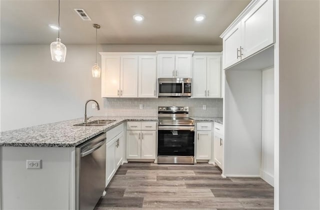 kitchen featuring appliances with stainless steel finishes, white cabinetry, decorative light fixtures, and sink