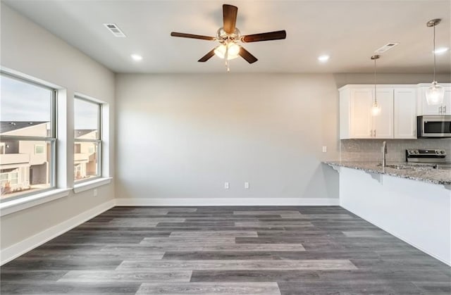 kitchen with light stone countertops, appliances with stainless steel finishes, dark hardwood / wood-style floors, and white cabinetry