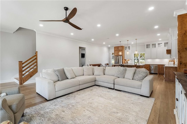 living room with light wood finished floors, recessed lighting, ornamental molding, ceiling fan, and stairs