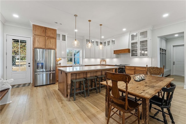 kitchen with appliances with stainless steel finishes, premium range hood, a kitchen island, and tasteful backsplash