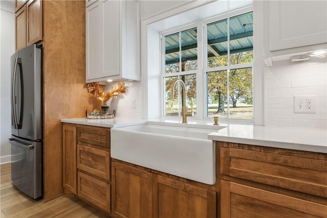 kitchen featuring brown cabinets, light countertops, light wood-style floors, freestanding refrigerator, and a sink