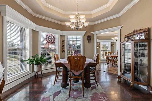 dining space featuring ornamental molding, dark wood-type flooring, a tray ceiling, and a notable chandelier