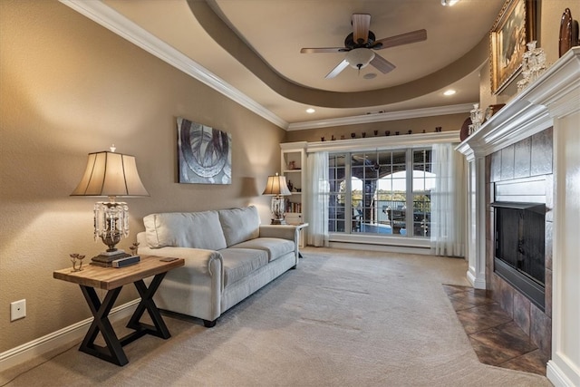 carpeted living room with a tiled fireplace, ceiling fan, crown molding, and a tray ceiling