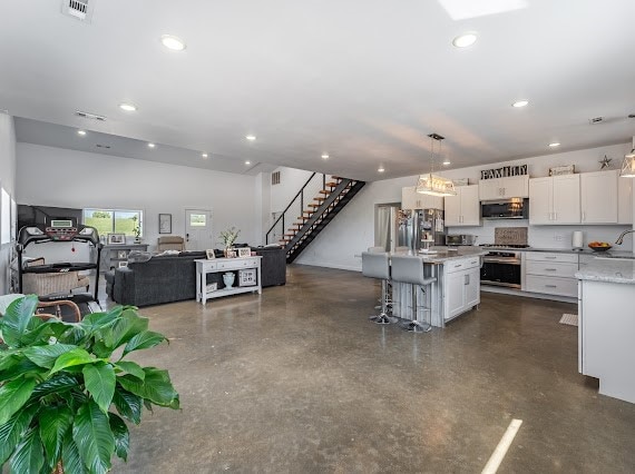 kitchen featuring appliances with stainless steel finishes, a center island, pendant lighting, white cabinets, and a breakfast bar area