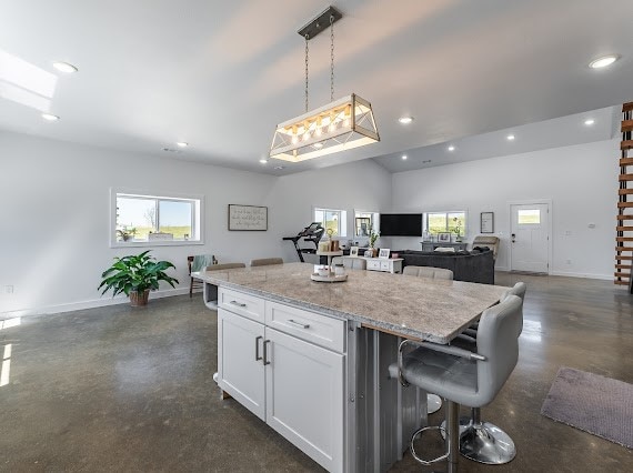 kitchen featuring a kitchen island, a kitchen breakfast bar, decorative light fixtures, white cabinets, and light stone counters