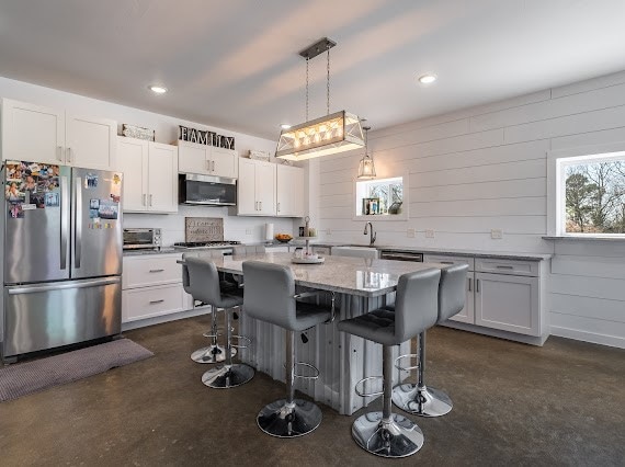 kitchen with a kitchen island, hanging light fixtures, white cabinetry, stainless steel appliances, and a breakfast bar area