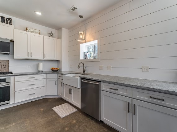 kitchen featuring sink, hanging light fixtures, white cabinetry, stainless steel appliances, and wooden walls