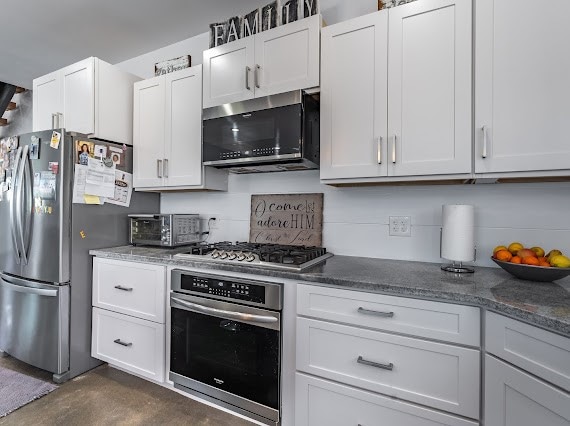 kitchen featuring dark stone countertops, stainless steel appliances, and white cabinets