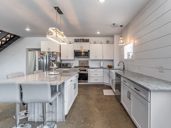 kitchen featuring a kitchen island, a breakfast bar, white cabinets, decorative light fixtures, and appliances with stainless steel finishes