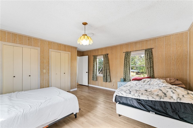 bedroom with a textured ceiling, multiple closets, wooden walls, and wood-type flooring