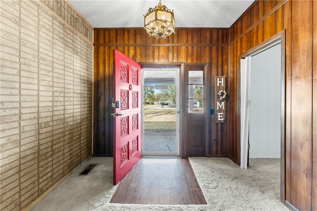 foyer entrance with carpet flooring, an inviting chandelier, and wood walls