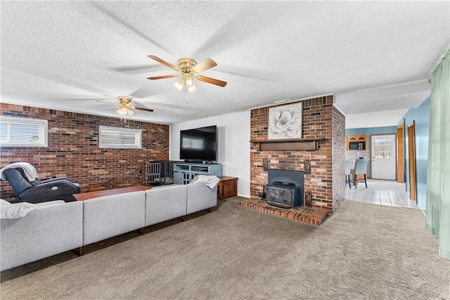 living room featuring a wood stove, a textured ceiling, light carpet, ceiling fan, and brick wall