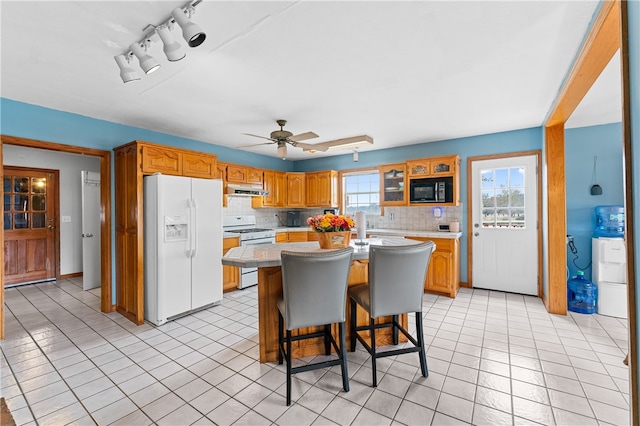 kitchen with a kitchen breakfast bar, backsplash, a center island, light tile patterned floors, and white appliances