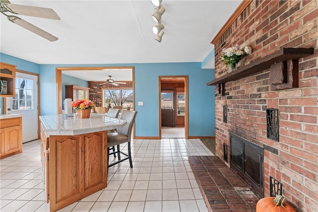 18405 Rheas Community Rd, Lincoln, AR 72744 - kitchen with a ceiling fan, tile countertops, a brick fireplace, light tile patterned floors, and baseboards