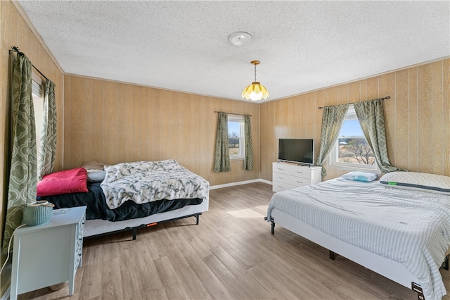 bedroom with light hardwood / wood-style floors, wood walls, and a textured ceiling