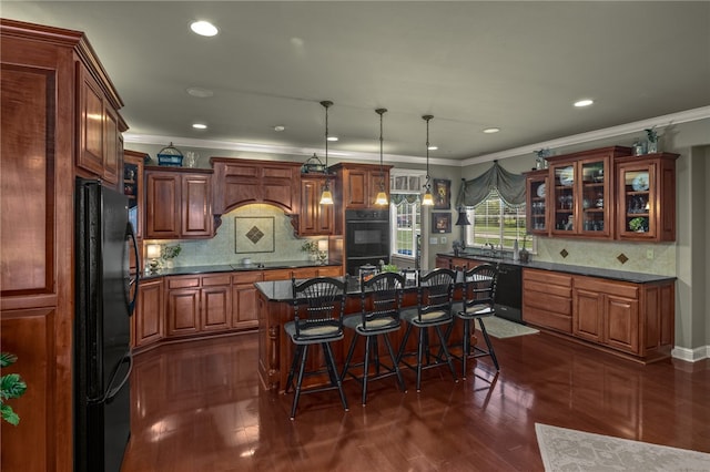 kitchen with a kitchen island, ornamental molding, black appliances, dark wood-type flooring, and pendant lighting