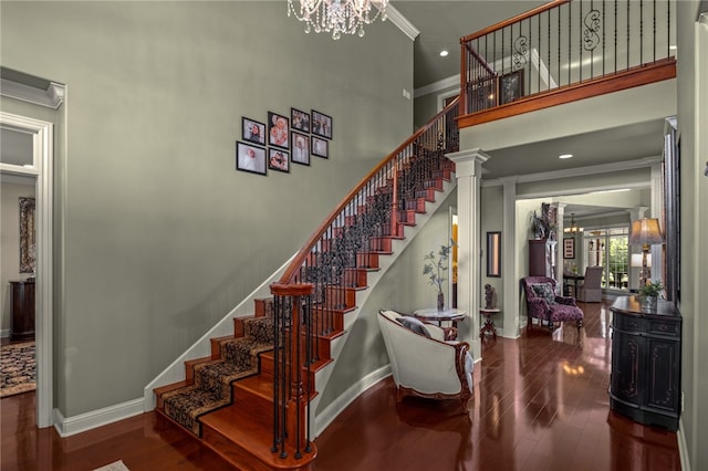 stairway featuring wood-type flooring, decorative columns, a high ceiling, crown molding, and a notable chandelier