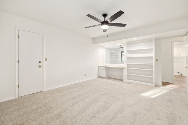 unfurnished living room featuring light carpet, built in desk, and ceiling fan