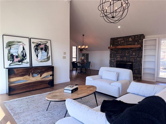 living room with hardwood / wood-style floors, lofted ceiling, a stone fireplace, and a notable chandelier