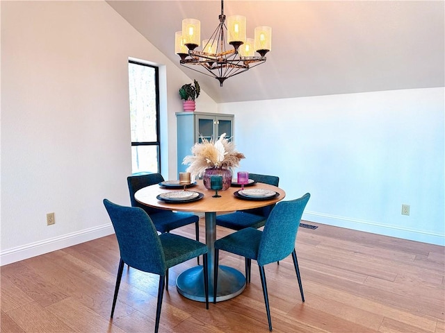 dining space with wood-type flooring, a chandelier, and vaulted ceiling