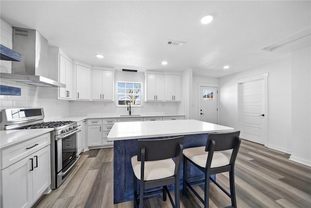 kitchen featuring wall chimney exhaust hood, gas stove, white cabinetry, dark hardwood / wood-style floors, and a kitchen island