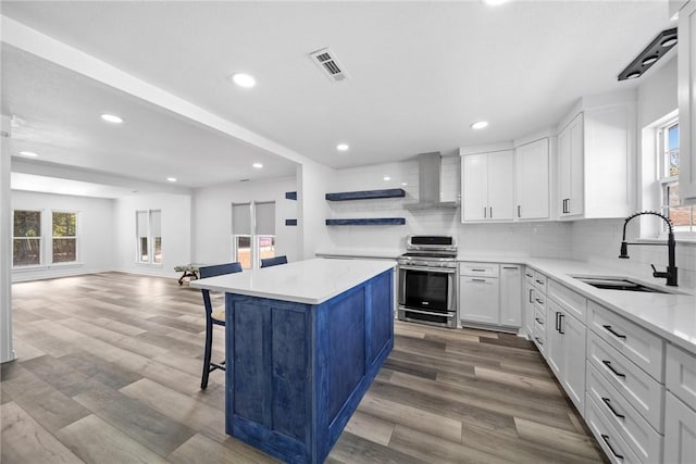 kitchen featuring wall chimney exhaust hood, sink, stainless steel range oven, white cabinets, and a center island