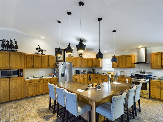 kitchen featuring a breakfast bar, pendant lighting, wall chimney range hood, and appliances with stainless steel finishes