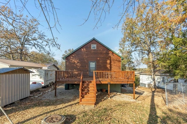 rear view of house featuring a storage shed, an outbuilding, a wooden deck, and fence