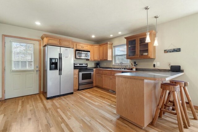 kitchen with kitchen peninsula, hanging light fixtures, a breakfast bar area, light hardwood / wood-style flooring, and stainless steel appliances