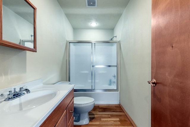 full bathroom featuring vanity, bath / shower combo with glass door, hardwood / wood-style flooring, and toilet