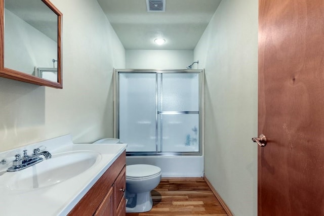 full bath featuring toilet, bath / shower combo with glass door, wood finished floors, vanity, and visible vents