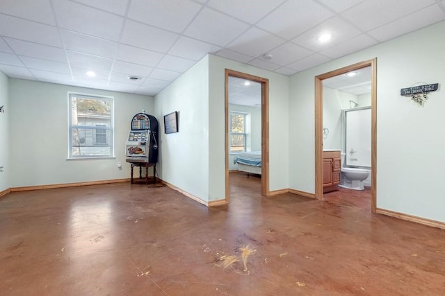 spare room with a paneled ceiling, finished concrete flooring, and baseboards