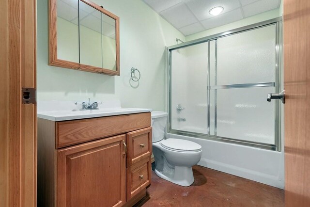 full bathroom with a drop ceiling, combined bath / shower with glass door, concrete flooring, toilet, and vanity